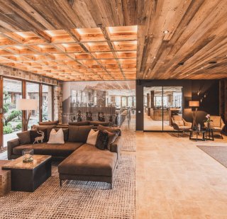 Pure - Ehrwald - Loungebereich Teppich gemustert, Beistelltische, Sofa braun, Zierkissen, Holzdecke